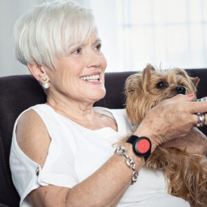 Femme avec son chien, assise sur le canapé, portant un bracelet de téléassistance