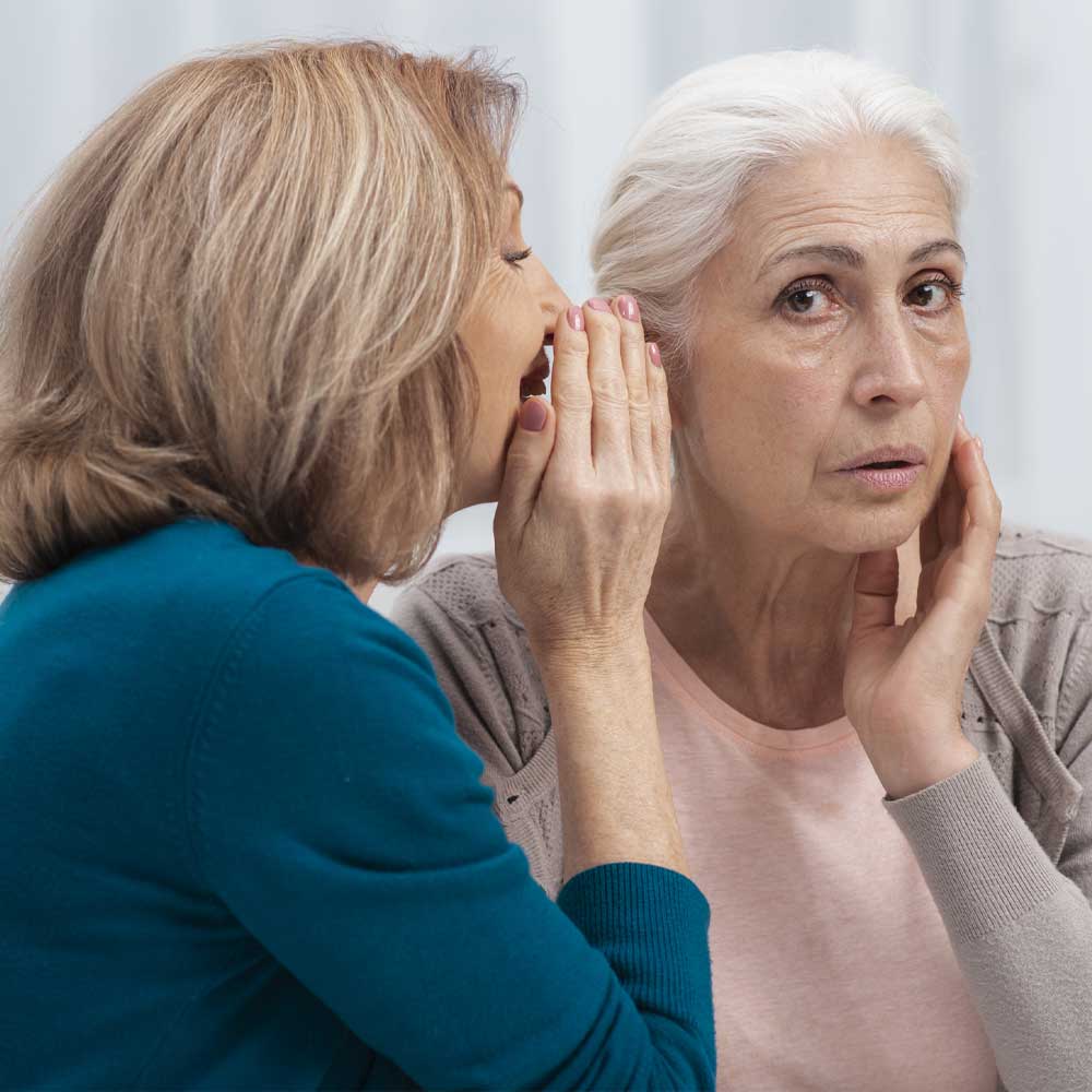 Une femme chuchote à l'oreille d'une senior souffrant d'acouphènes