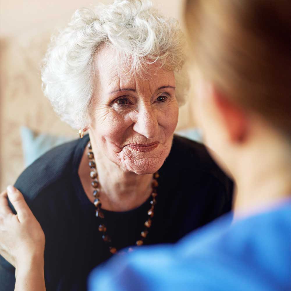 Une vieille dame évaluée en Gir 2, son aide-soignante a la main sur son épaule