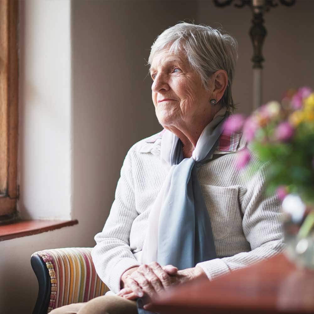 Une femme senior à domicile, évaluée en Gir 3, elle regarde par sa fenêtre