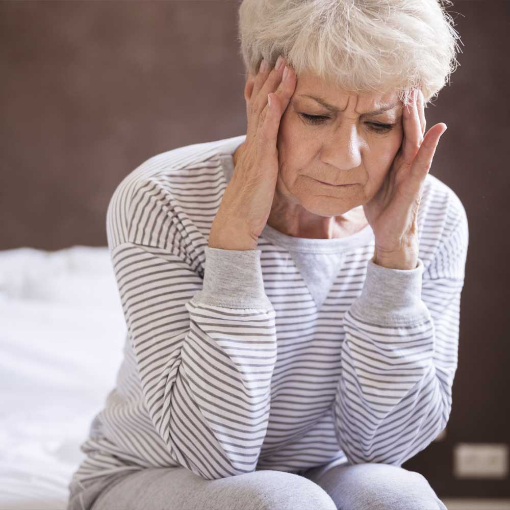 Une femme senior assise au bord de son lit, elle prend sa tête entre ses mains, elle souffre d'une leucopathie dégénérative